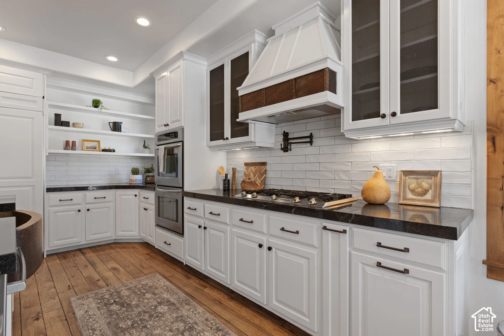 White cabinetry with black hardware, dark countertops, wood-finish flooring, a built-in oven, and a gas range