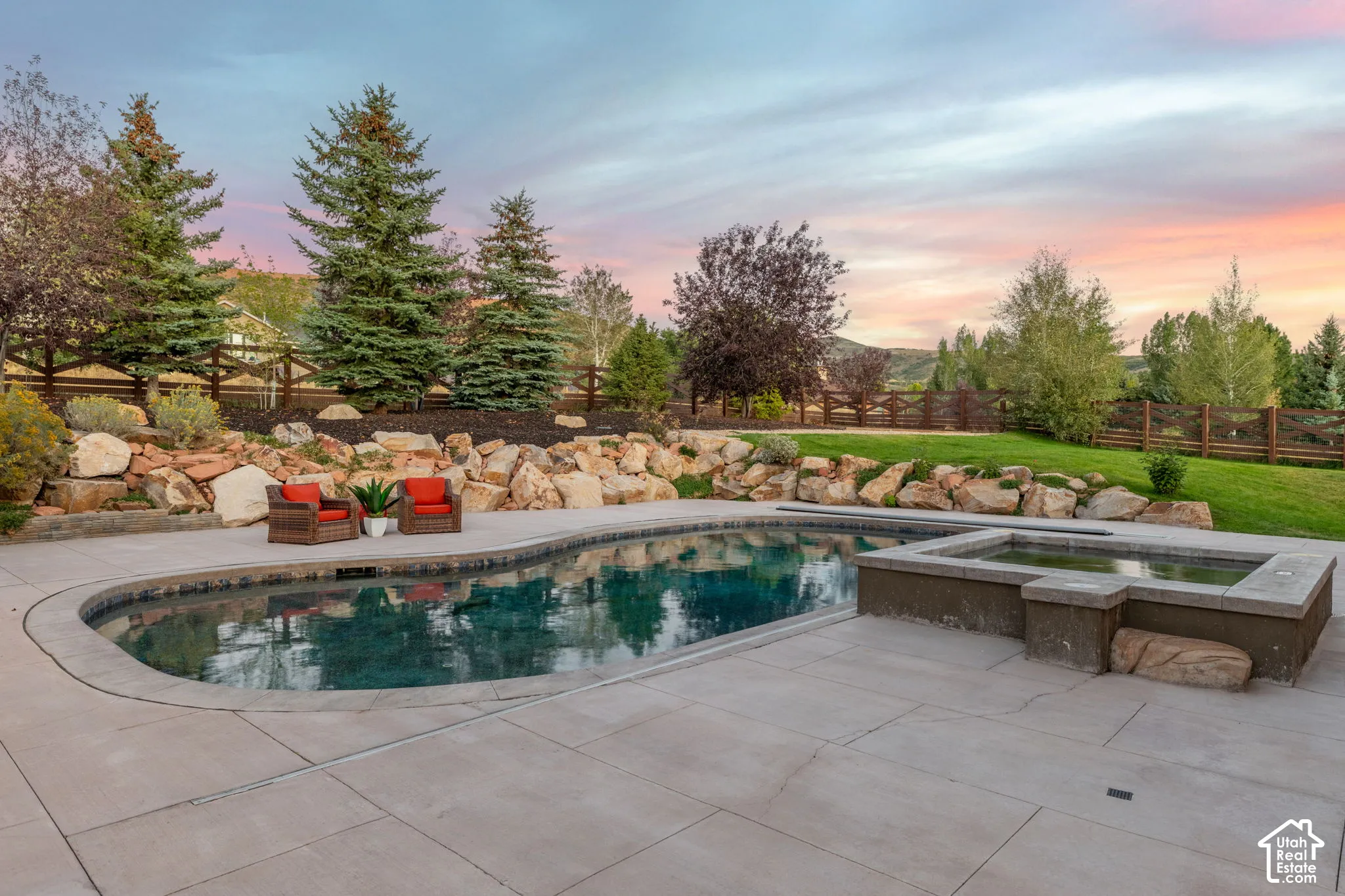 Curved swimming pool with integrated spa, concrete decking, and natural rock landscaping