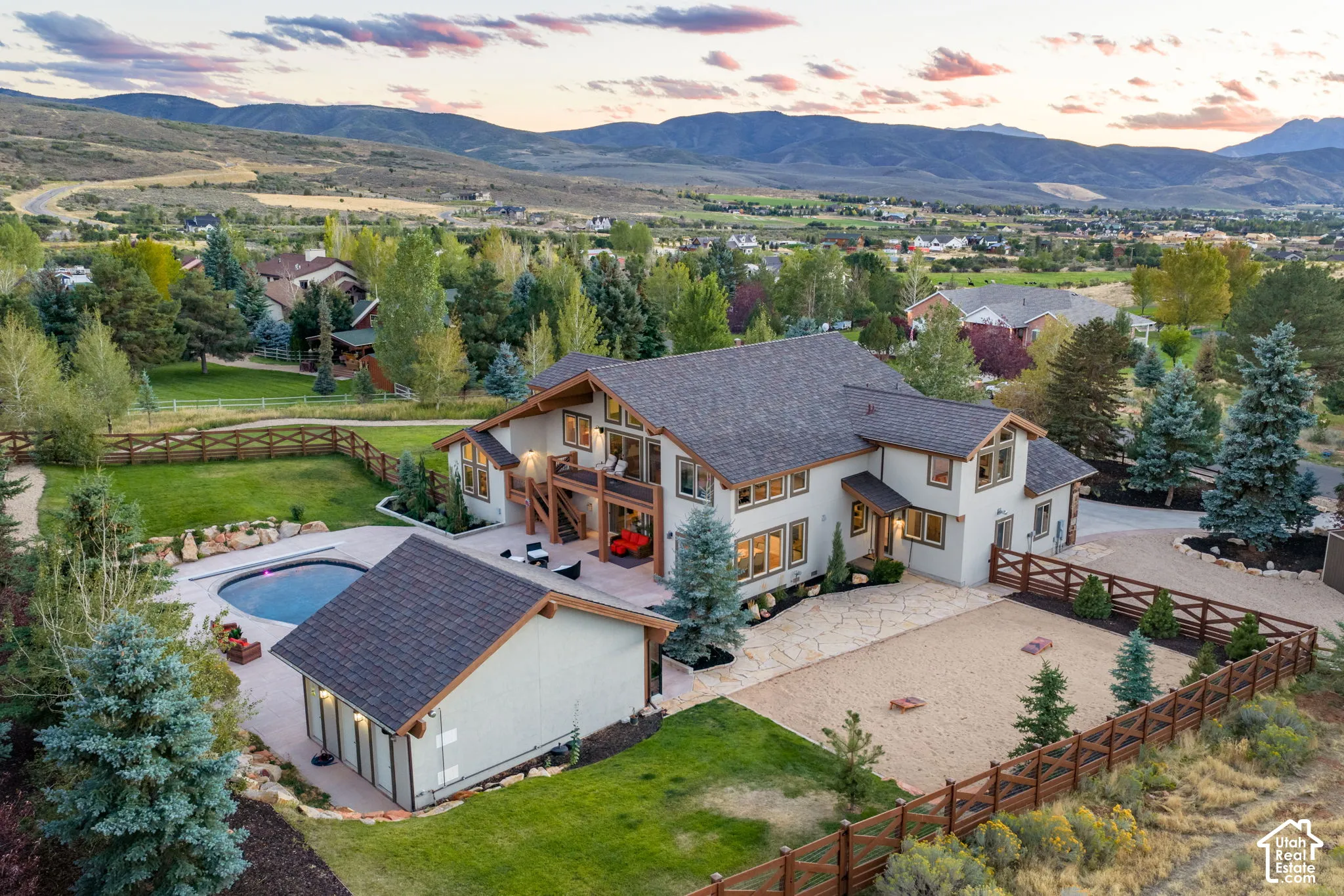 Stucco exterior with wood trim accents, expansive gravel driveway, fenced perimeter, in-ground swimming pool, and detached auxiliary structure