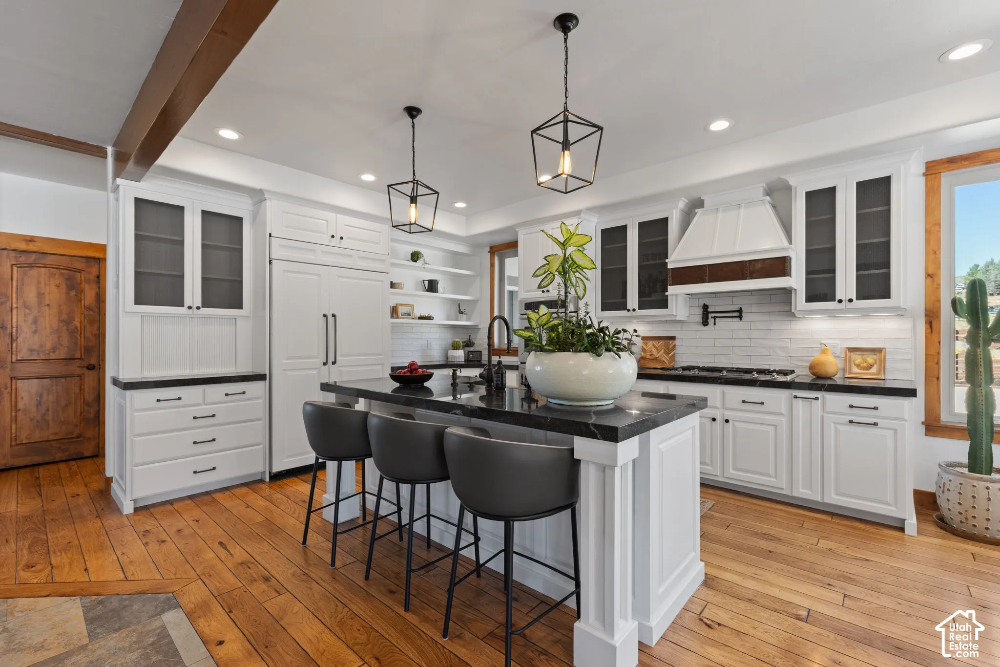 Spacious kitchen featuring an island with stone countertop, white shaker cabinetry, wood-finish flooring, and a white subway tile backsplash