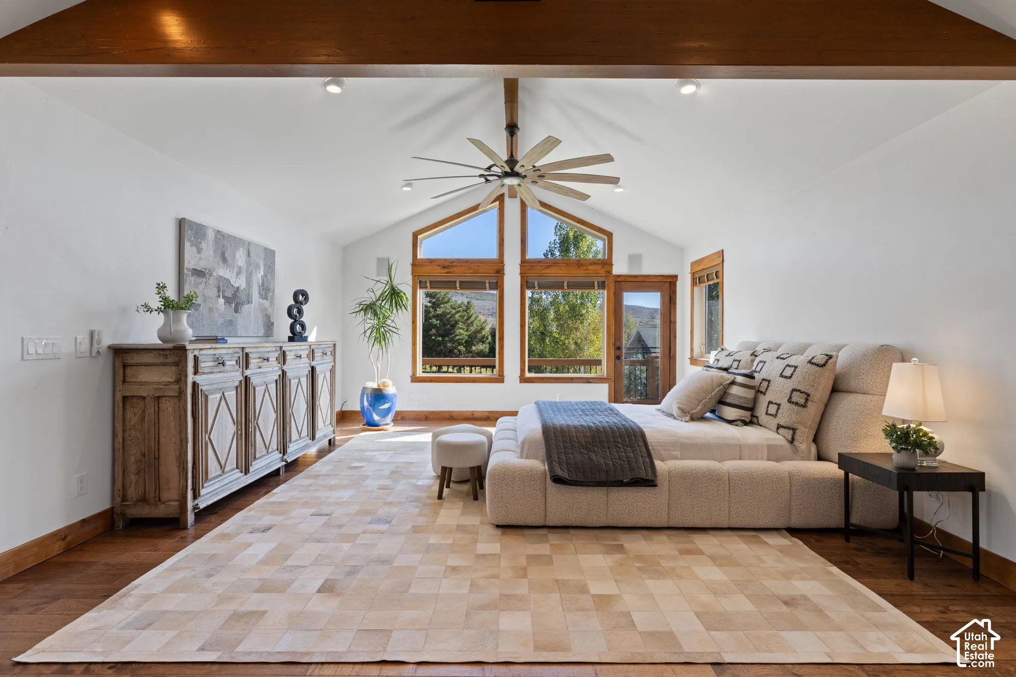Vaulted ceilings with exposed wood beams, wood-finish flooring, a ceiling fan, and large windows with wood frames