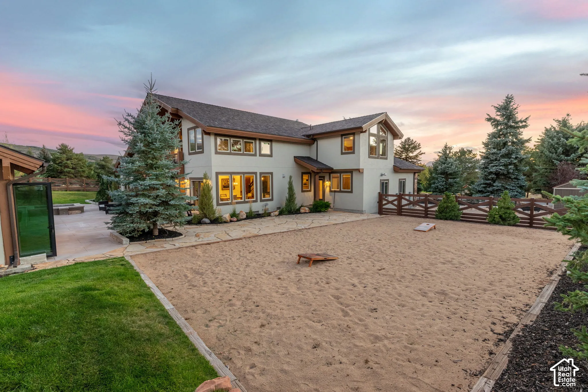 Exterior residence featuring a sand court, established landscaping, stone paving, and a wooden fence