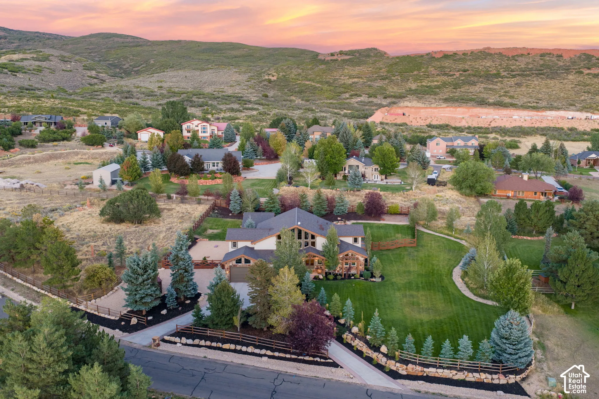 Expansive property featuring a manicured lawn, paved driveway, mature trees, and a stone retaining wall