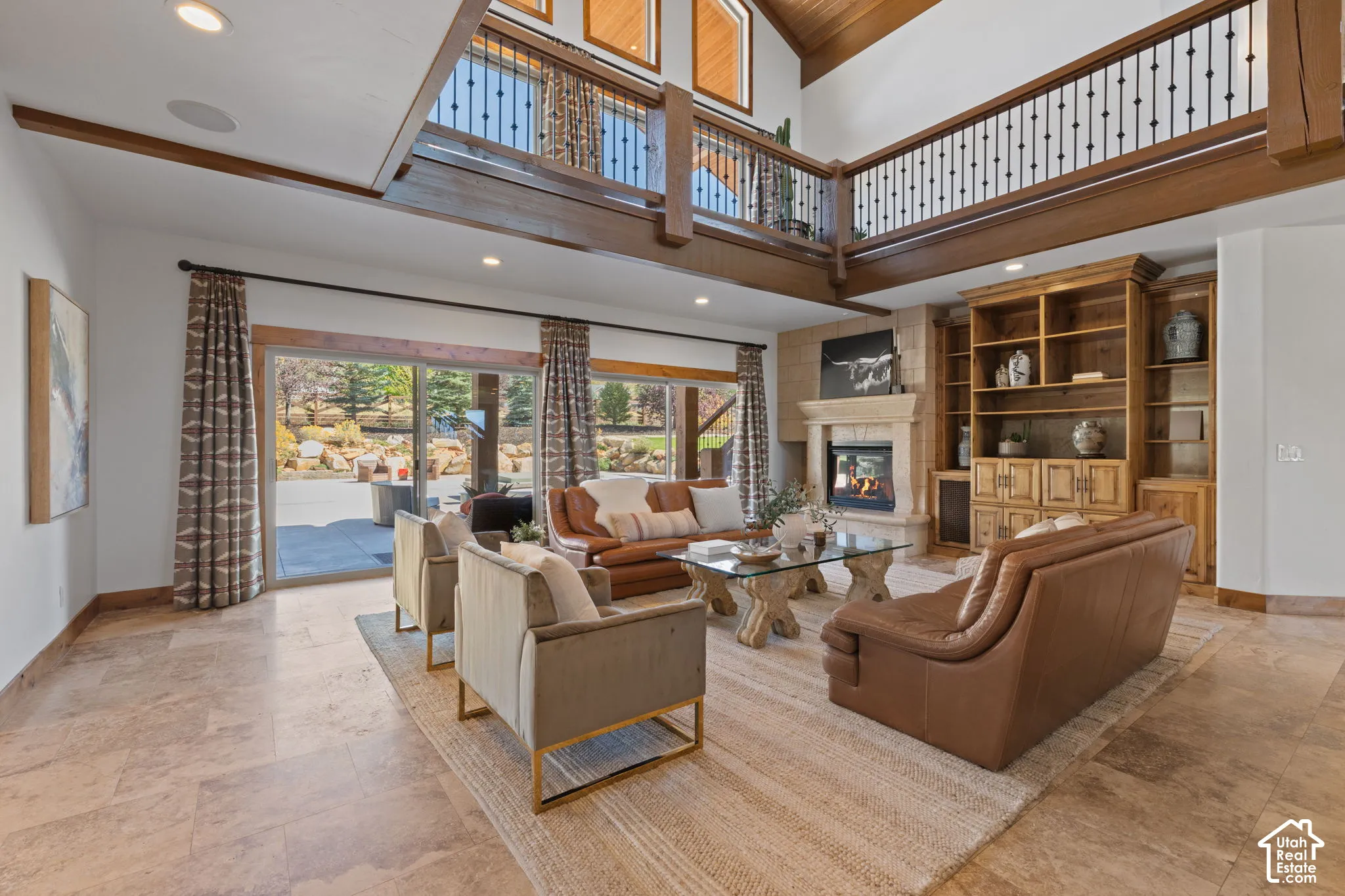 Vaulted ceilings with exposed wood beams, a stone fireplace, built-in wooden shelving, sliding glass doors, and tiled flooring