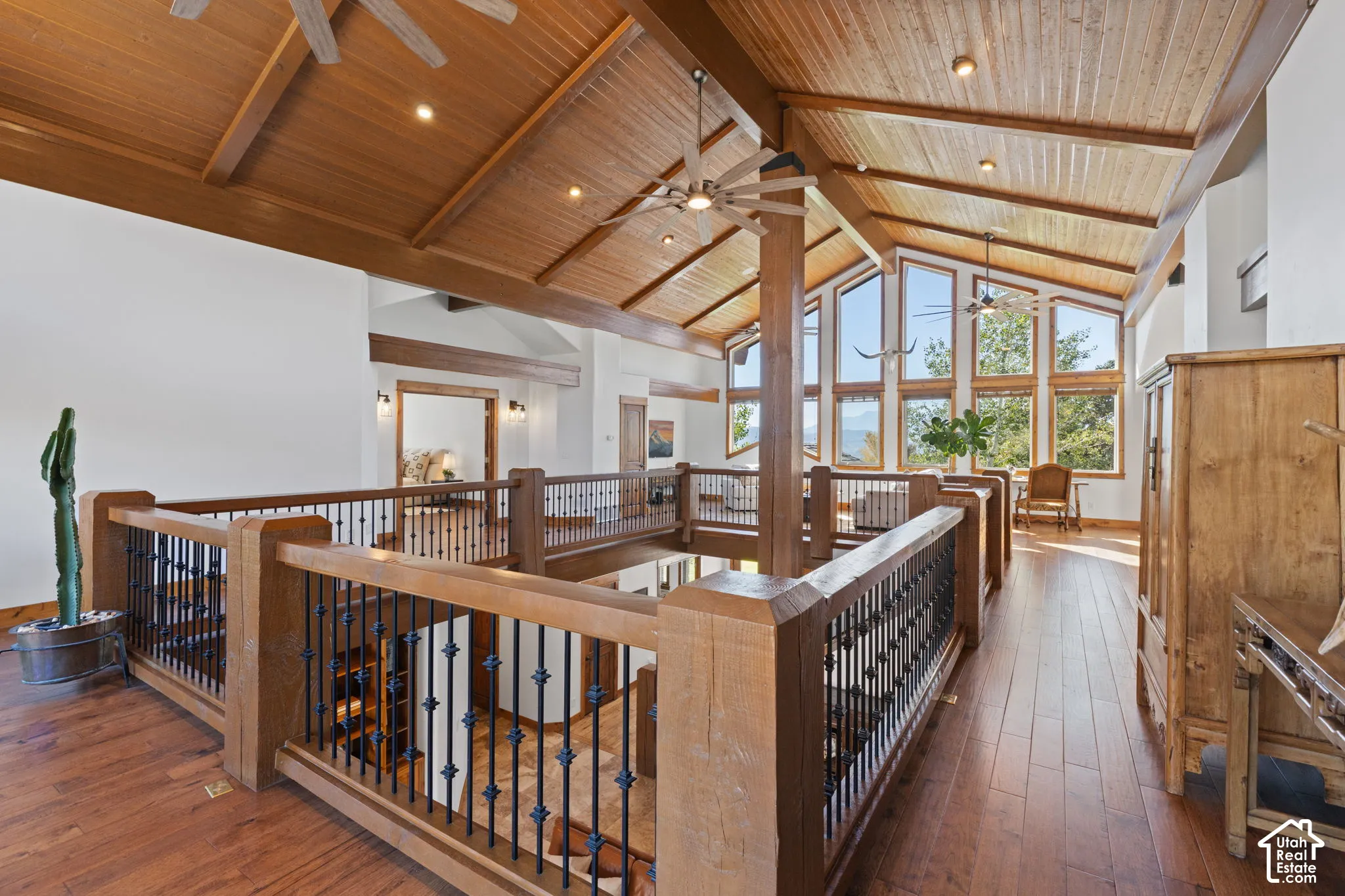 Vaulted wood-paneled ceiling with exposed beams, wood-finish flooring, custom wood and wrought iron railings, and multiple large windows