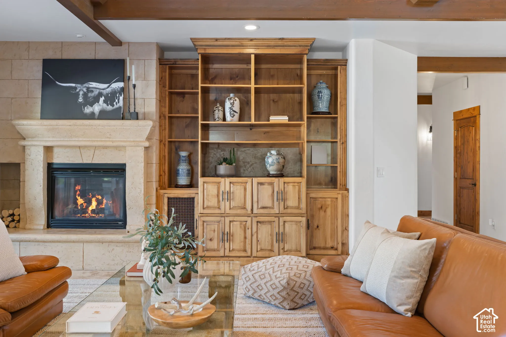 Stone-clad fireplace with mantel, built-in shelving, exposed ceiling beams, and wood-paneled door