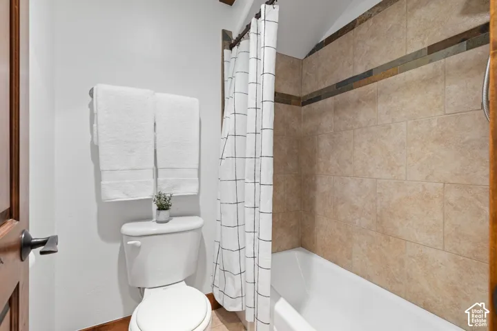 Tiled shower surround with decorative accent band, white bathtub, and wood-finish door with dark hardware