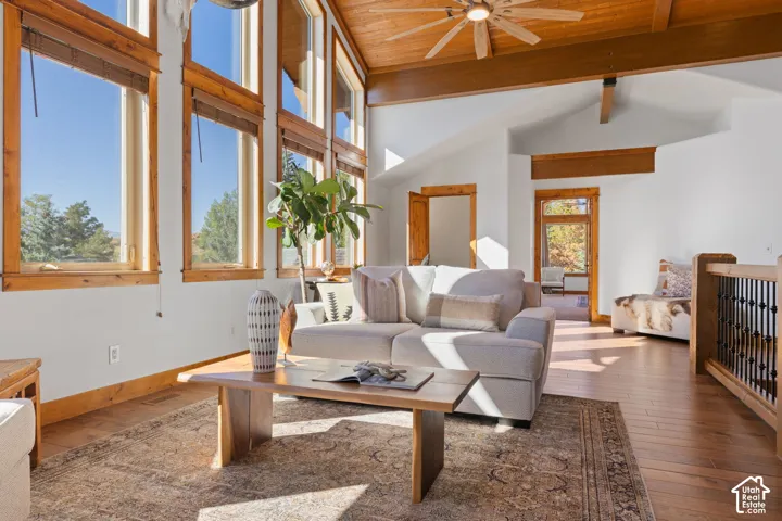 Vaulted ceiling with wood-finish planks and exposed beams, wood-finish flooring, full-height windows, and a ceiling fan