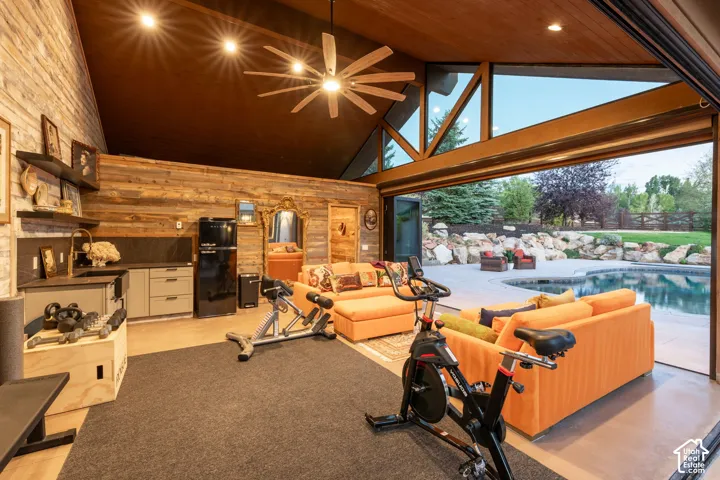 Vaulted wood-paneled ceiling, exposed beam construction, large-format glass doors, outdoor swimming pool, and stone-accented exterior landscaping