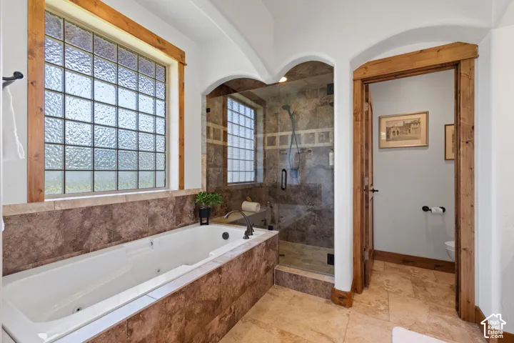 Soaking tub with tiled surround, walk-in shower with glass enclosure, wood-trimmed privacy window, and wood-framed doorway
