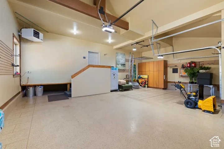 Spacious garage featuring a durable finished floor, built-in wooden cabinetry, wall-mounted storage tracks, a built-in bench, and exposed ceiling beams