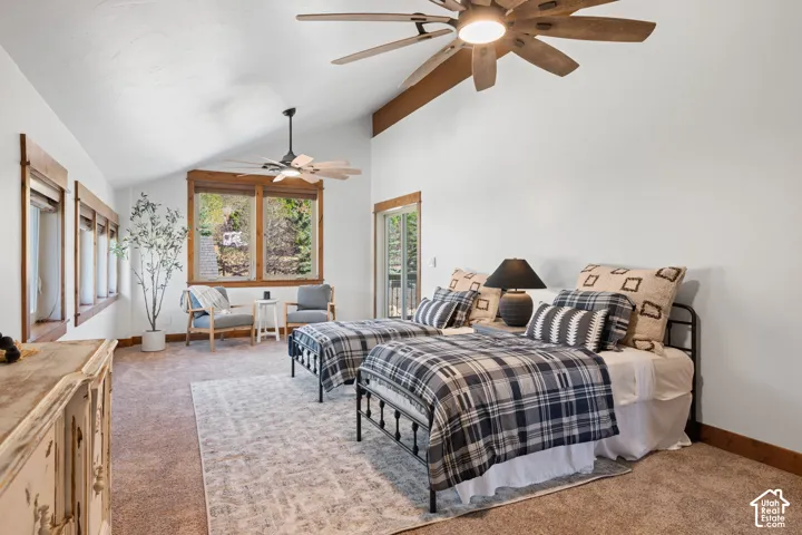 Vaulted ceiling with exposed wood beam, ceiling fans, multiple windows with wood trim, glass-paneled door, and carpeted flooring