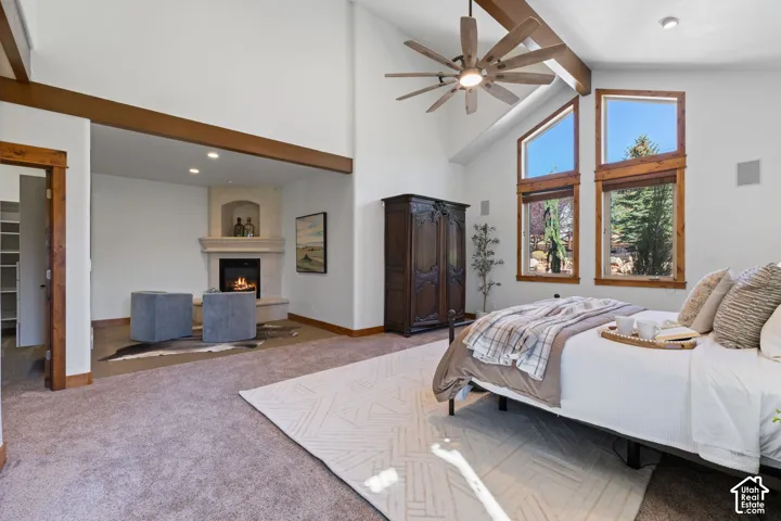 Vaulted ceilings with exposed wood beams, corner fireplace with stone surround, large wood-framed windows, and a ceiling fan