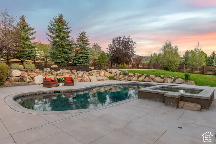 Curved swimming pool with integrated spa, concrete decking, and natural rock landscaping