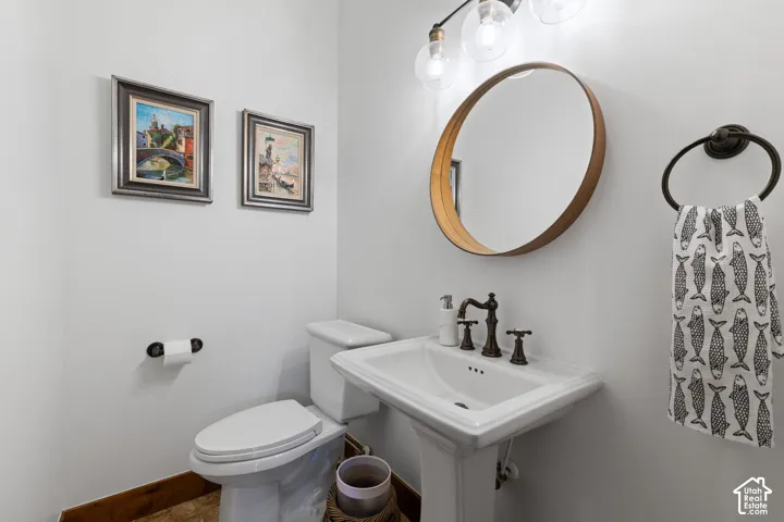 Pedestal sink with dark bronze fixtures, circular mirror with wood-finish frame, and overhead vanity lighting