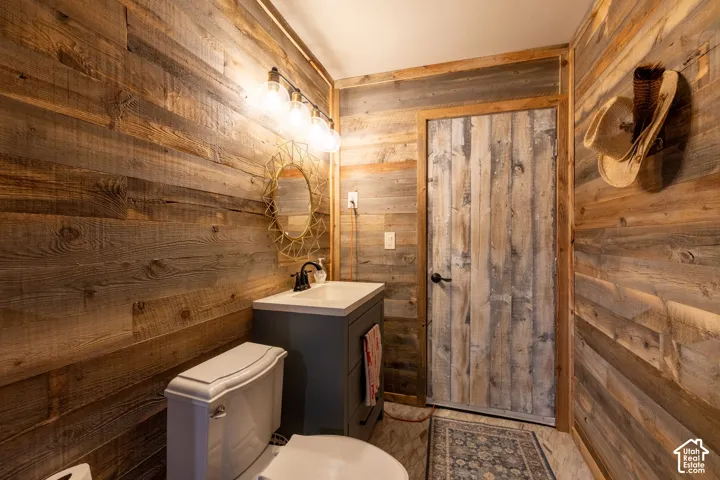 Distressed wood paneling, vanity with a white countertop, vanity light fixture, decorative mirror, and a white toilet