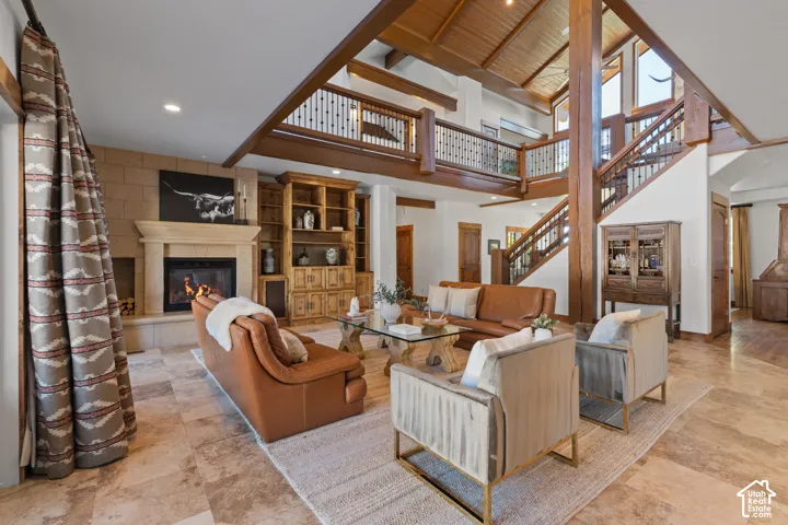 Vaulted wood-paneled ceiling, stone-clad fireplace, integrated wood shelving, exposed wood beams, and a wood staircase with iron balusters