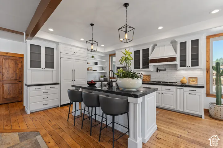 Spacious kitchen featuring an island with stone countertop, white shaker cabinetry, wood-finish flooring, and a white subway tile backsplash