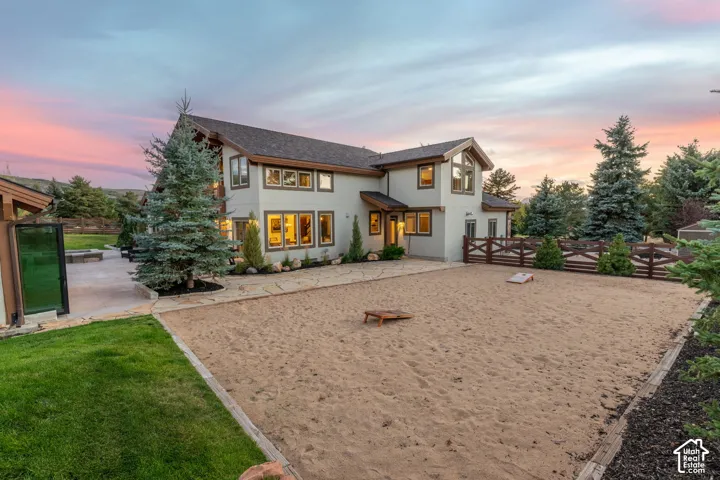 Exterior residence featuring a sand court, established landscaping, stone paving, and a wooden fence