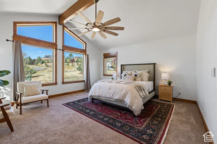 Vaulted ceiling with wood beam accents, expansive picture windows, wood-finish window frames, ceiling fan with integrated lighting, and carpeted flooring