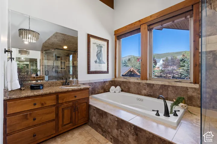 Built-in soaking tub with dark-finished fixtures, dual windows with wood trim, and a vanity with wood cabinetry and a stone-finish countertop