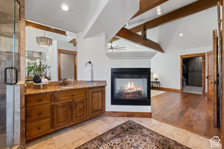 Built-in fireplace, exposed wood beams, wood-finish flooring, glass-enclosed shower, and wood vanity with stone countertop