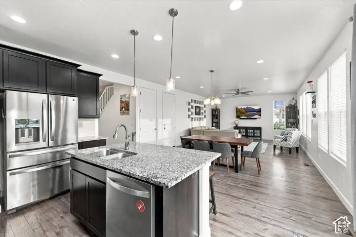 Open-concept living area featuring wood-finish flooring, a kitchen island with granite countertops, stainless steel appliances, recessed lighting, and ample natural light from multiple windows