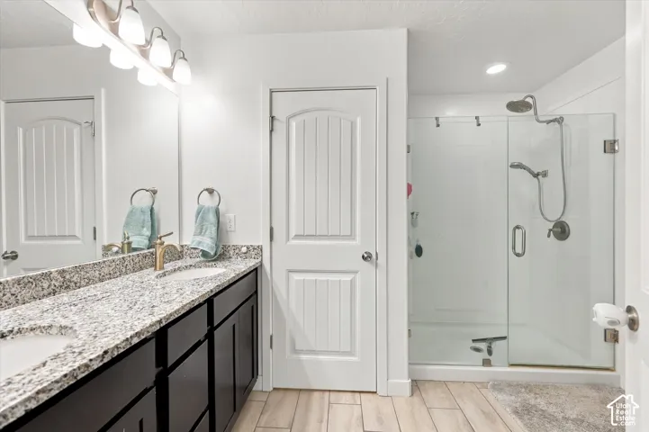 Dual vanity with granite countertop and undermount sinks, wood-finish flooring, glass-enclosed shower, and built-in recessed lighting