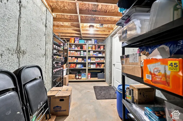 Unfinished basement space featuring exposed wood joists and concrete walls, with built-in shelving and a white door
