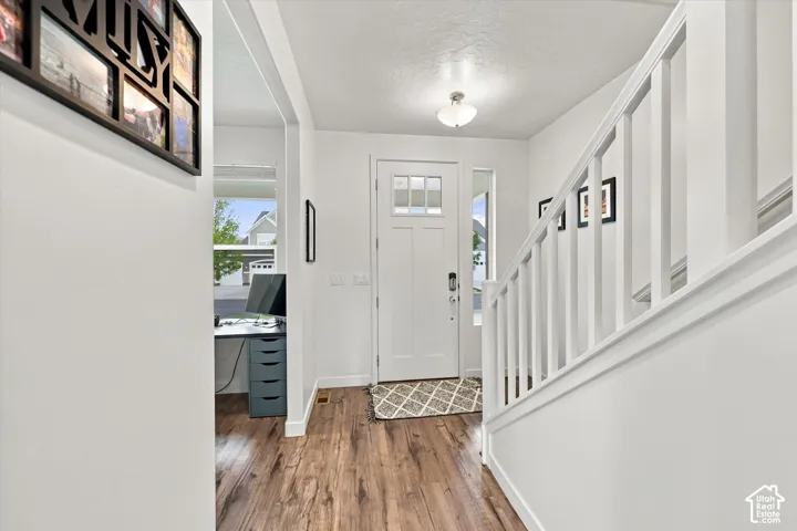Wood-finish flooring, white painted staircase, and a front entry door with glass paneling