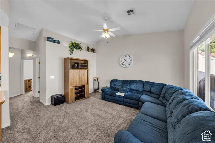 Vaulted ceiling, ceiling fan, neutral wall tones, carpet flooring, and large sliding glass door