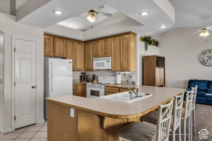 Kitchen featuring wood cabinetry, white appliances, a breakfast bar with seating, recessed lighting, and a vaulted ceiling