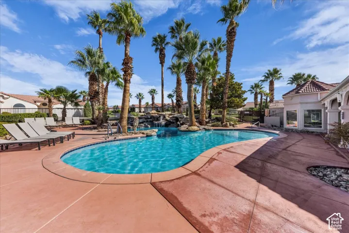 Expansive swimming pool with integrated rock waterfall feature, surrounded by mature palm trees and concrete decking