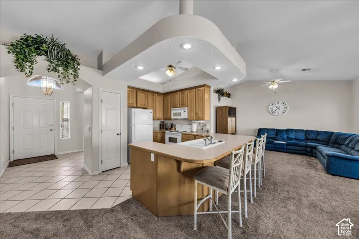 Open-concept kitchen and living area featuring vaulted ceilings, recessed lighting, wood cabinetry, a breakfast bar, and an integrated kitchen island with a double basin sink