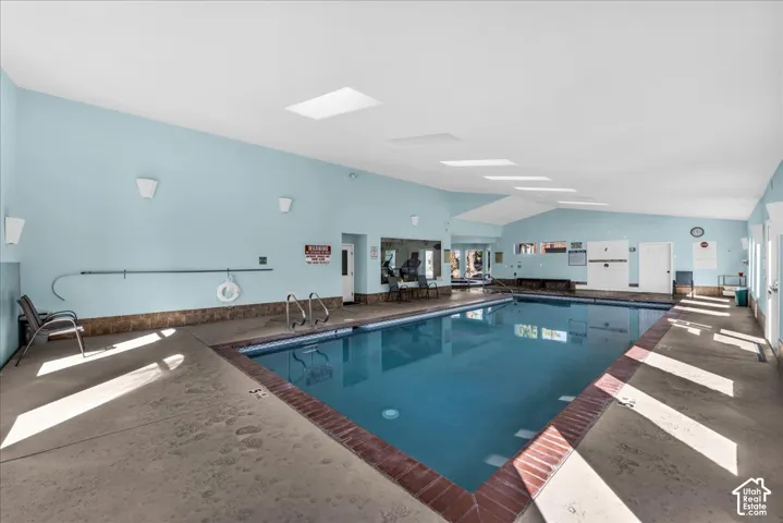 Indoor swimming pool featuring a brick coping, vaulted ceiling, and multiple skylights