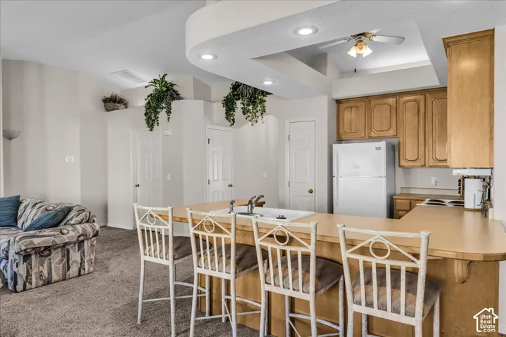 Kitchen featuring wood cabinetry, white appliances, and a breakfast bar with seating