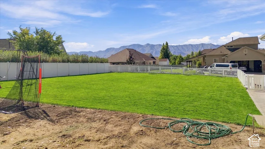 Expansive lawn area, white privacy fence, white picket fence, mountain backdrop, and clear sky
