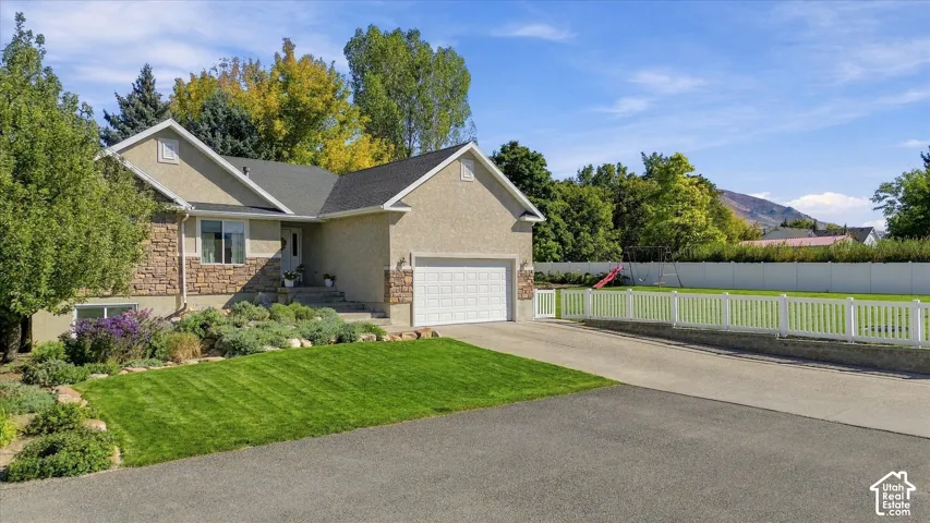 Stucco and stone exterior, attached two-car garage, manicured lawn, paved driveway, and white picket fencing