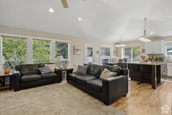 Open-concept living area featuring multiple large windows with natural light, hardwood flooring throughout, black leather sectional seating, pendant lighting fixtures, and seamless integration with a kitchen featuring white cabinetry and a center island w