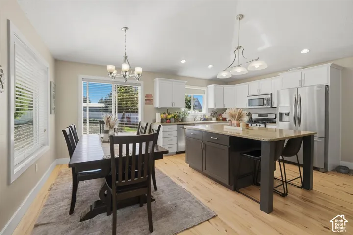 Kitchen featuring wood-finish flooring, white cabinetry, stainless steel appliances, and a central island with a light-toned countertop