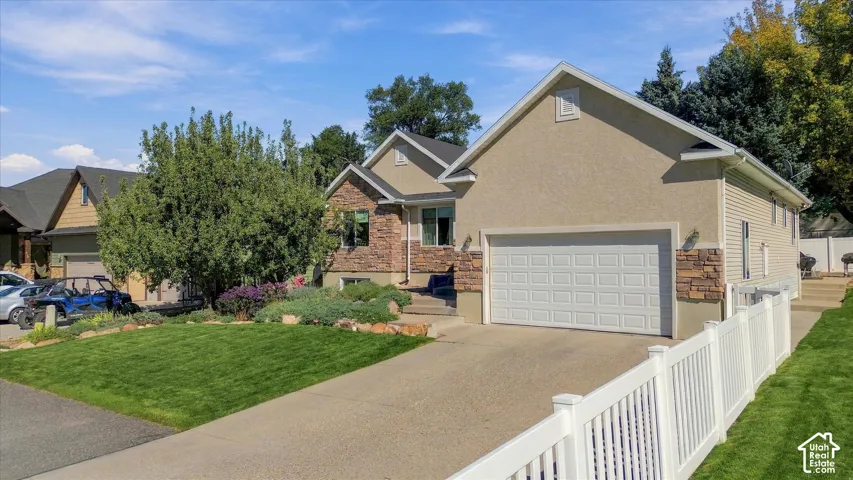 Stucco and stone exterior with a two-car garage, concrete driveway, and white picket fence