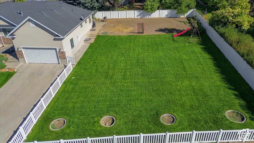 Expansive green lawn with a white privacy fence and a paved driveway