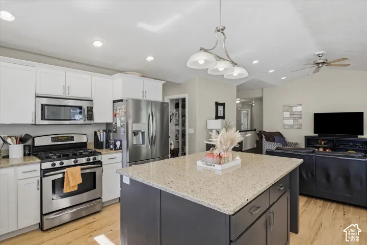 Kitchen featuring an island with stone-look countertop, stainless steel appliances, and white cabinetry