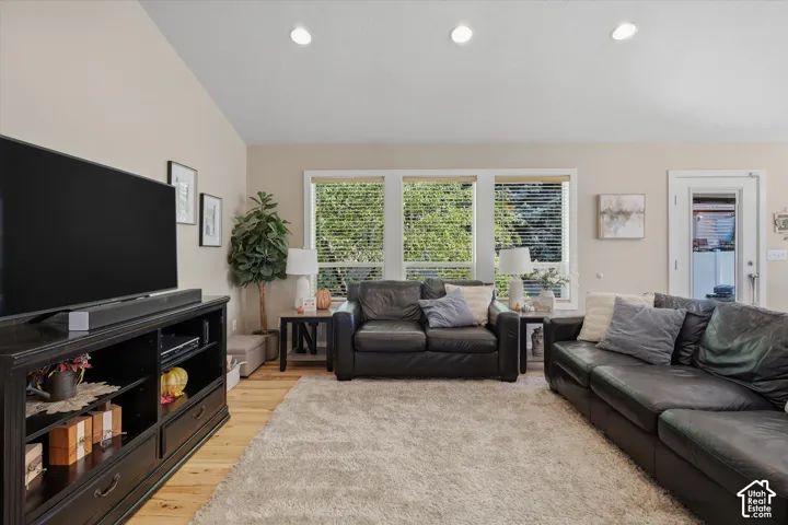 Vaulted ceiling, recessed lighting, wood-finish flooring, multiple windows with blinds, and white trim throughout