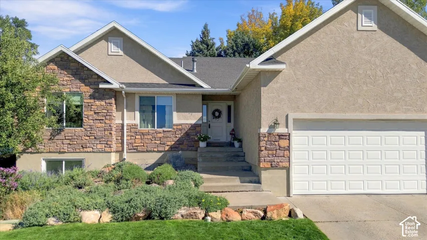 Stucco and stone exterior, attached two-car garage, front entry with concrete steps, and established landscaping