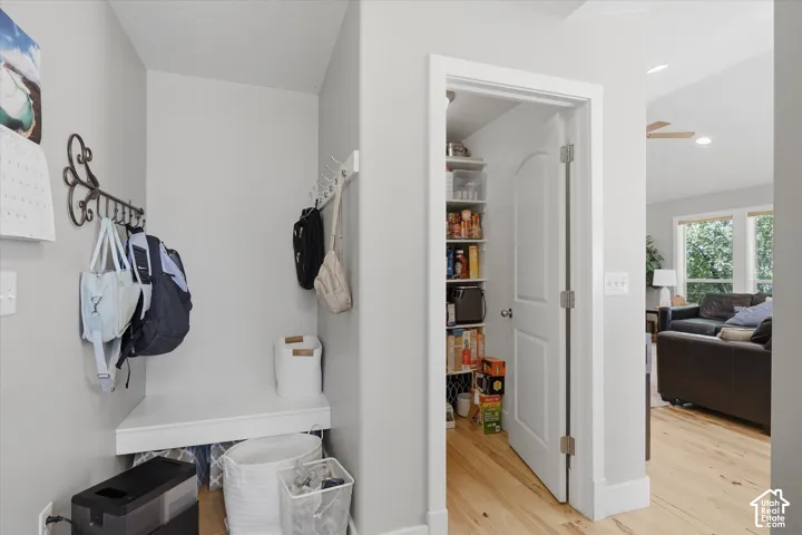 Built-in white bench seating, wall-mounted coat hooks, recessed lighting, wood-finish flooring, and a pantry with shelving