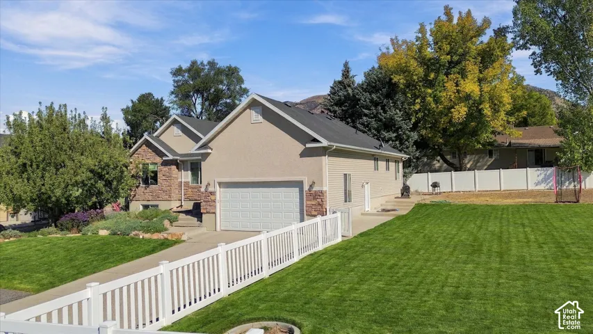 Stucco and stone facade, attached garage, concrete driveway, white picket fence, expansive green lawn