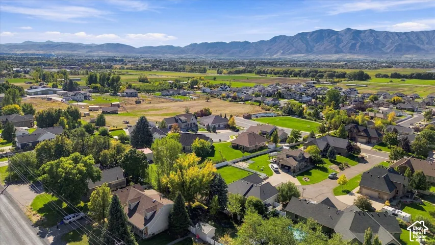 Expansive residential development with established landscaping, surrounded by open green fields and distant mountains