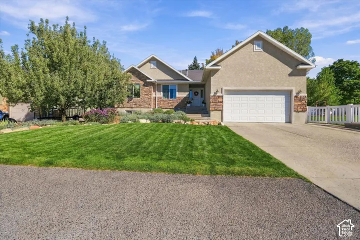 Stucco and stone exterior with an attached garage, featuring a concrete driveway, a manicured lawn, and mature trees