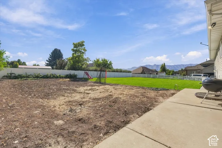 Expansive backyard with a concrete patio, a substantial area of manicured lawn, and a white privacy fence